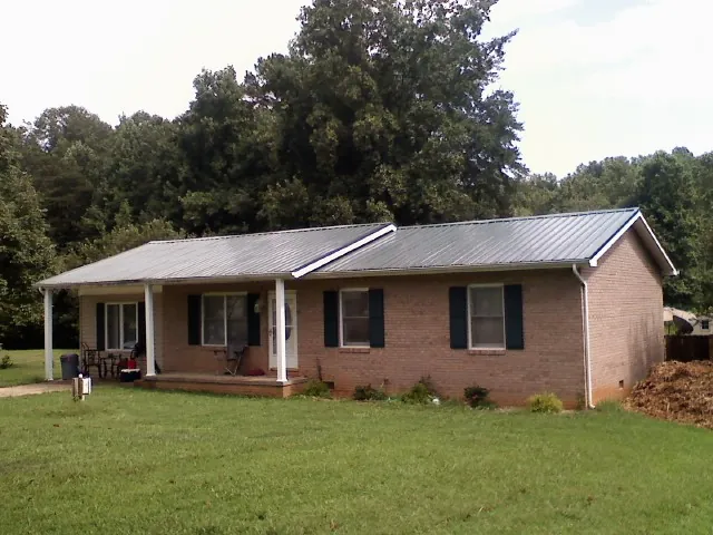 Gray metal roof on a brick ranch house with a side carport in Hastings